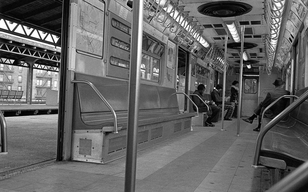 A subway train sits with it's doors open at the 82nd Street subway station in Corona, Queens as commuters enter and sit down, 1974.