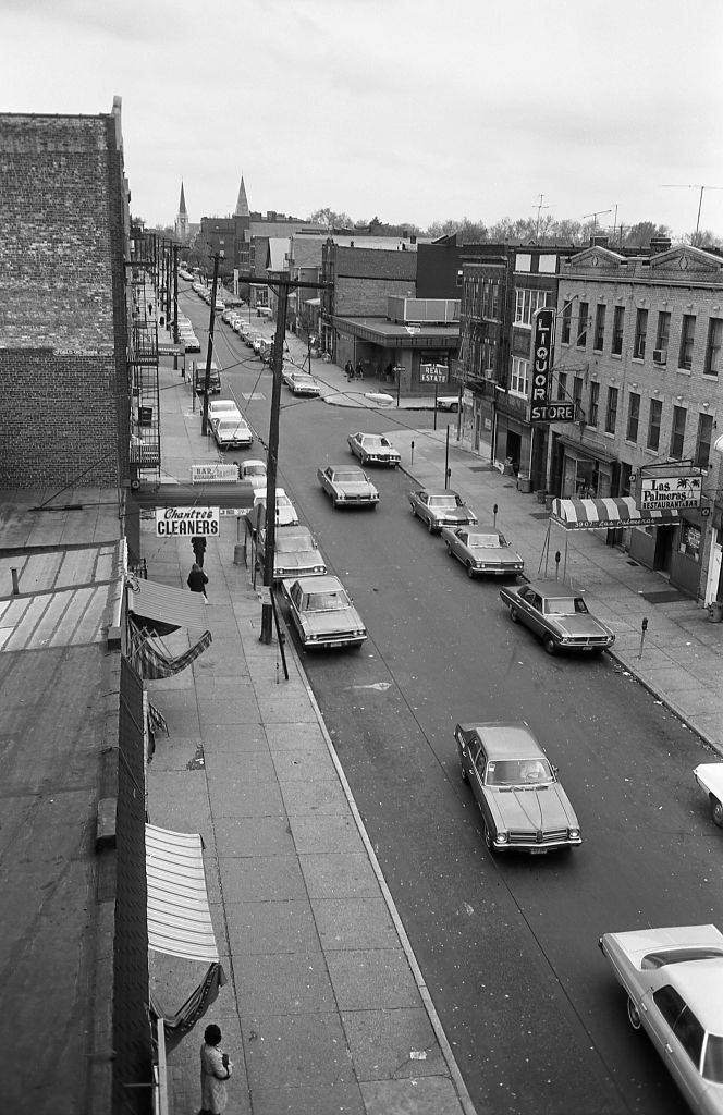Elevated subway line of a street lined with small businesses in Corona, Queens, 1974.