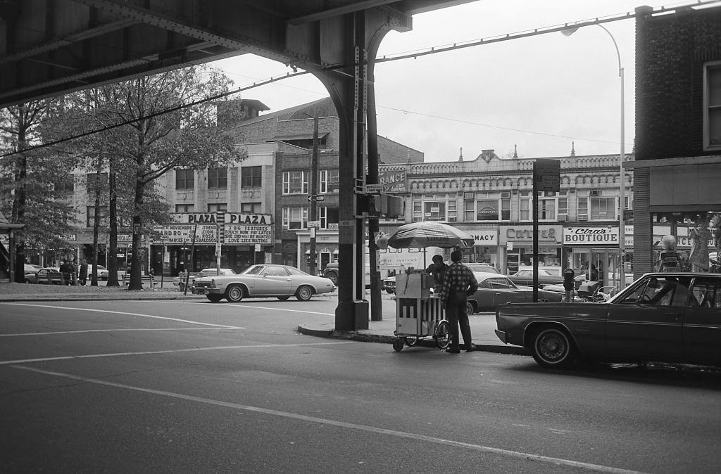 The Plaza Movie Theater, and other small businesses along Roosevelt Avenue in Corona, Queens, 1974.