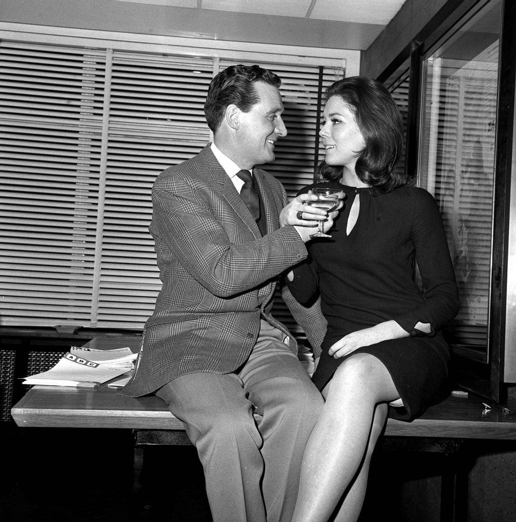 Diana Rigg and Patrick Macnee sitting on a table, 1965.