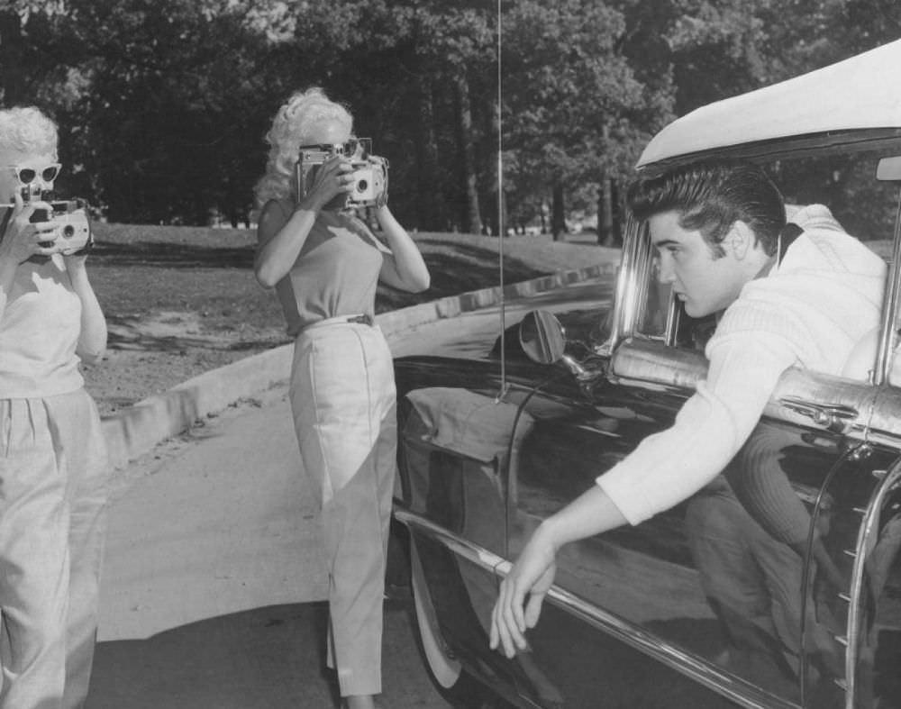 Always the ladies’ man, Elvis poses for two women with cameras in the driveway at Graceland while behind the wheel of his 1956 Cadillac Eldorado convertible.