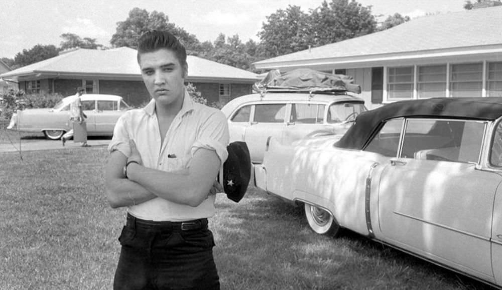 This photo was taken outside the Audubon home after Elvis had returned from a tour, 1956. Notice the band’s gear still strapped to the car in the background. The Pink Cadillac is behind Elvis, too.