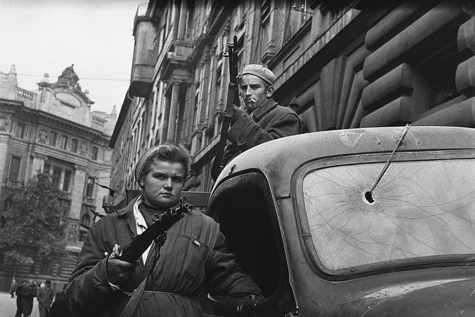Two Hungarian freedom fighters stand armed by a truck in Budapest during the Hungarian Revolution of 1956.