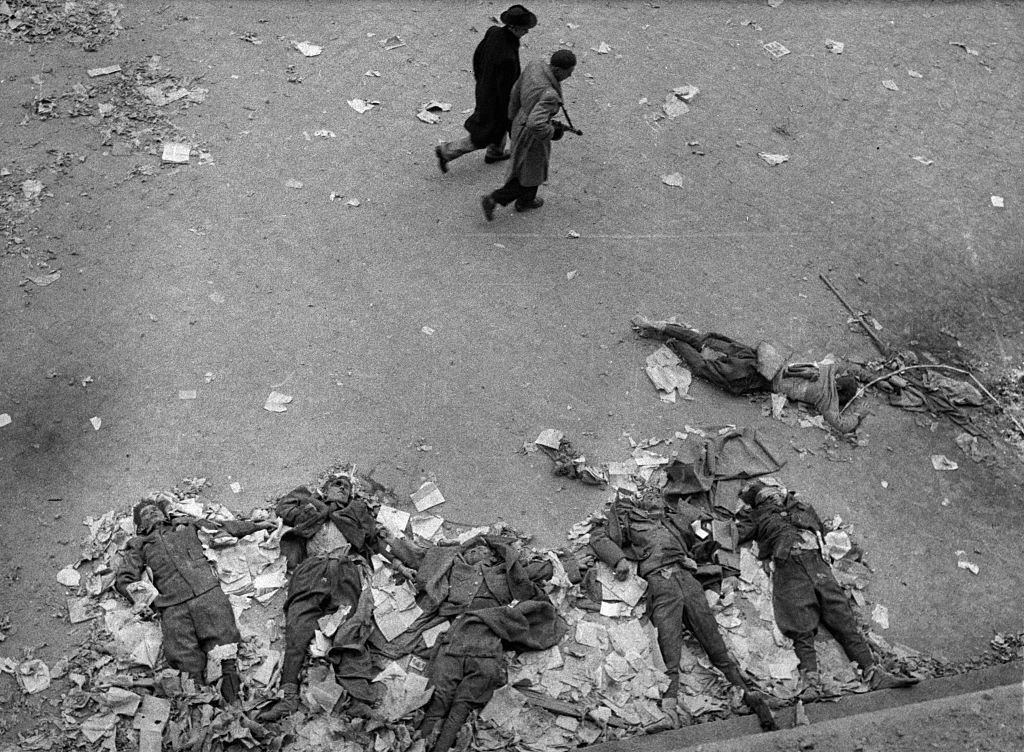 Two Hungarian soldiers walk past the deceased bodies of Soviet secret police during the anti-Communist revolution.