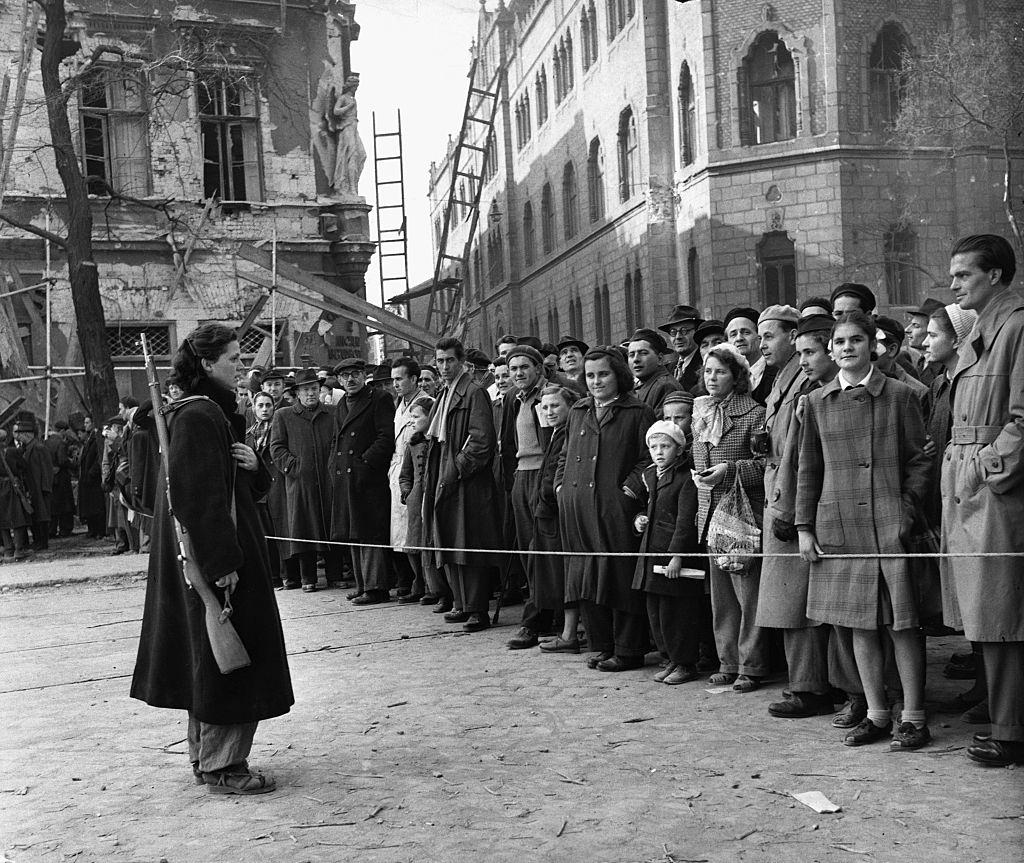 A woman patriot keeps back the crowds from the war zone.