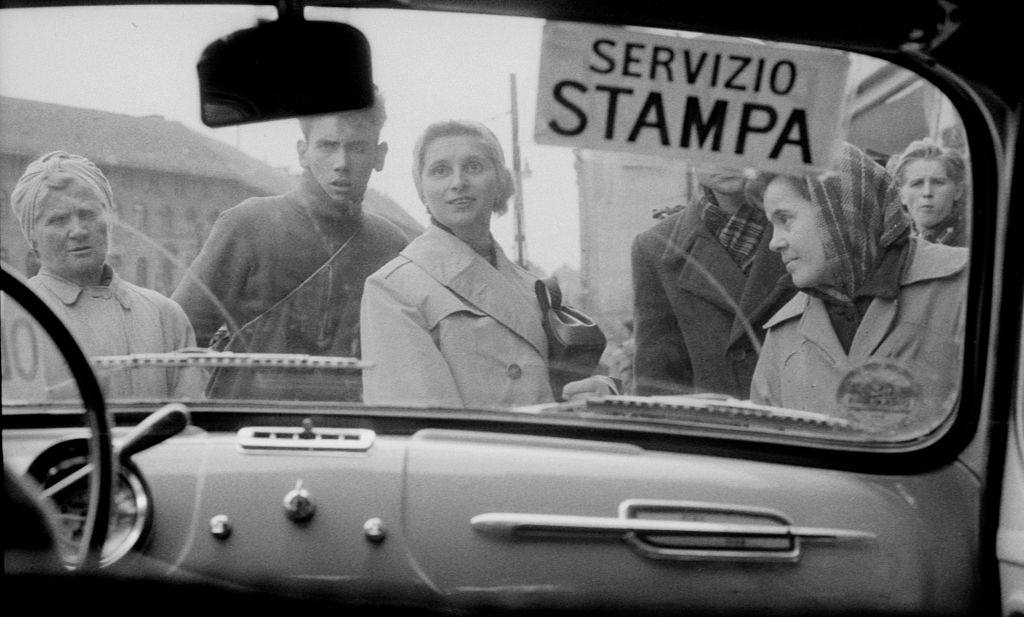 The crowd peeks inside the car of the journalist Massimo Mauri and the photographer Mario De Biasi just arrived in the Hungarian city to document the uprising against Soviet regime.