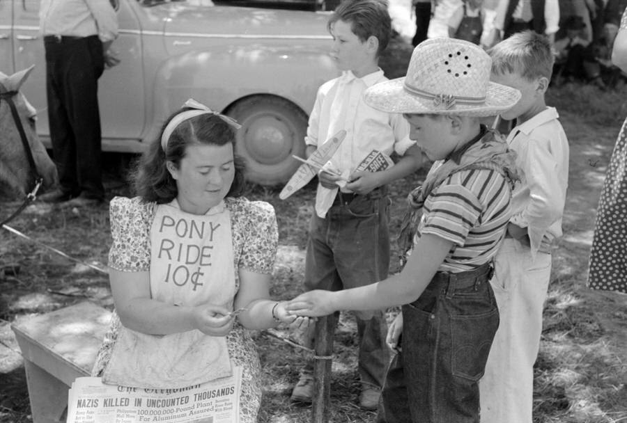 Ticket taker for pony ride concession. The headline on the Oregonian in her lap reads "Nazis Killed in Uncounted Thousands - Berezina River Runs With Blood."