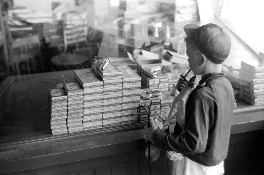 A boy looks in a store window at Hubley brand cap guns, in 'Army', 'Dick', and 'Cowboy' models, on the fourth of July in Vale.