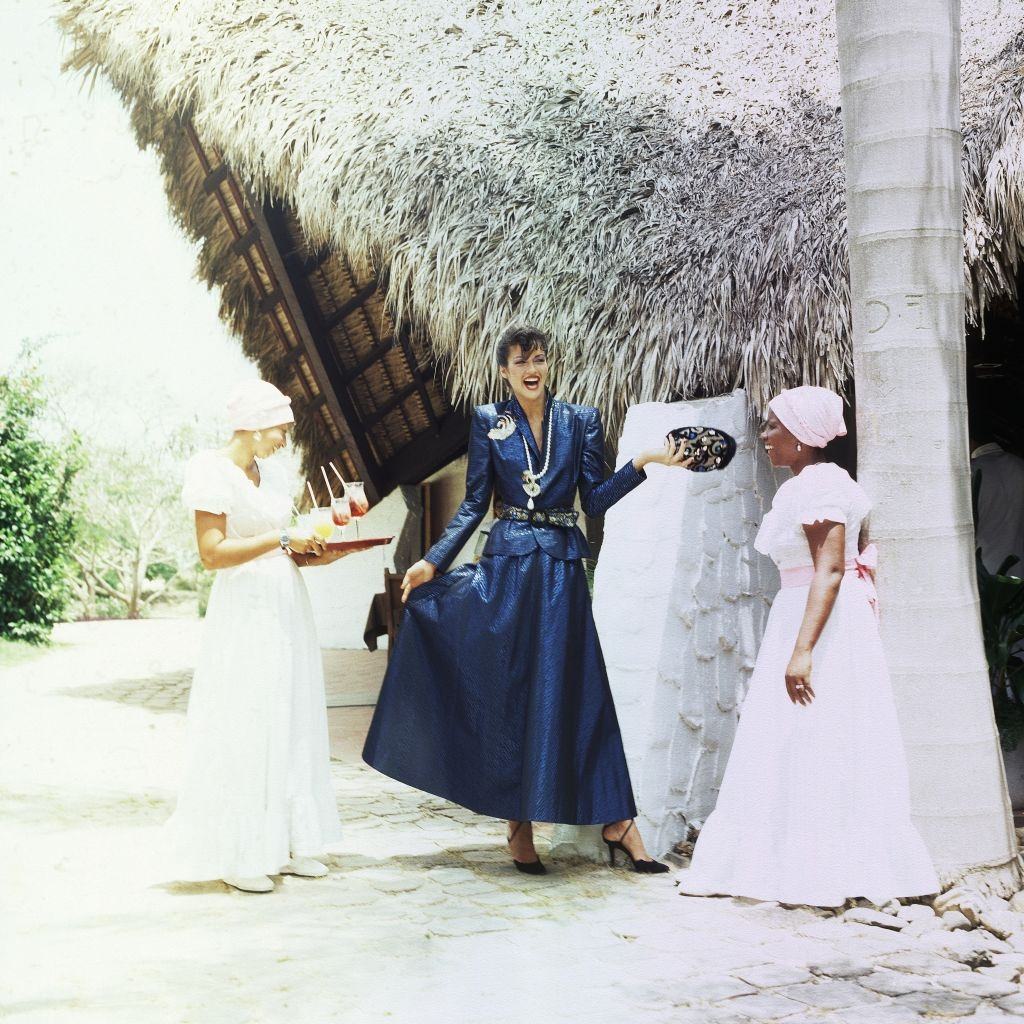 Janice Dickinson in The Dominican Republic wearing a long blue skirt and matching jacket, 1979.