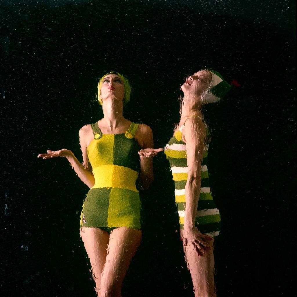 Jean Patchett n a yellow, green, and white striped swimsuit and matching swim cap with another model, 1960.