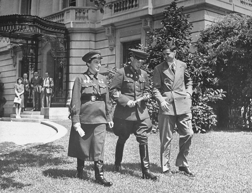 Lyudmila Pavlichenko walking across the lawn in front of the Russian Embassy with two gentlemen, 1942.