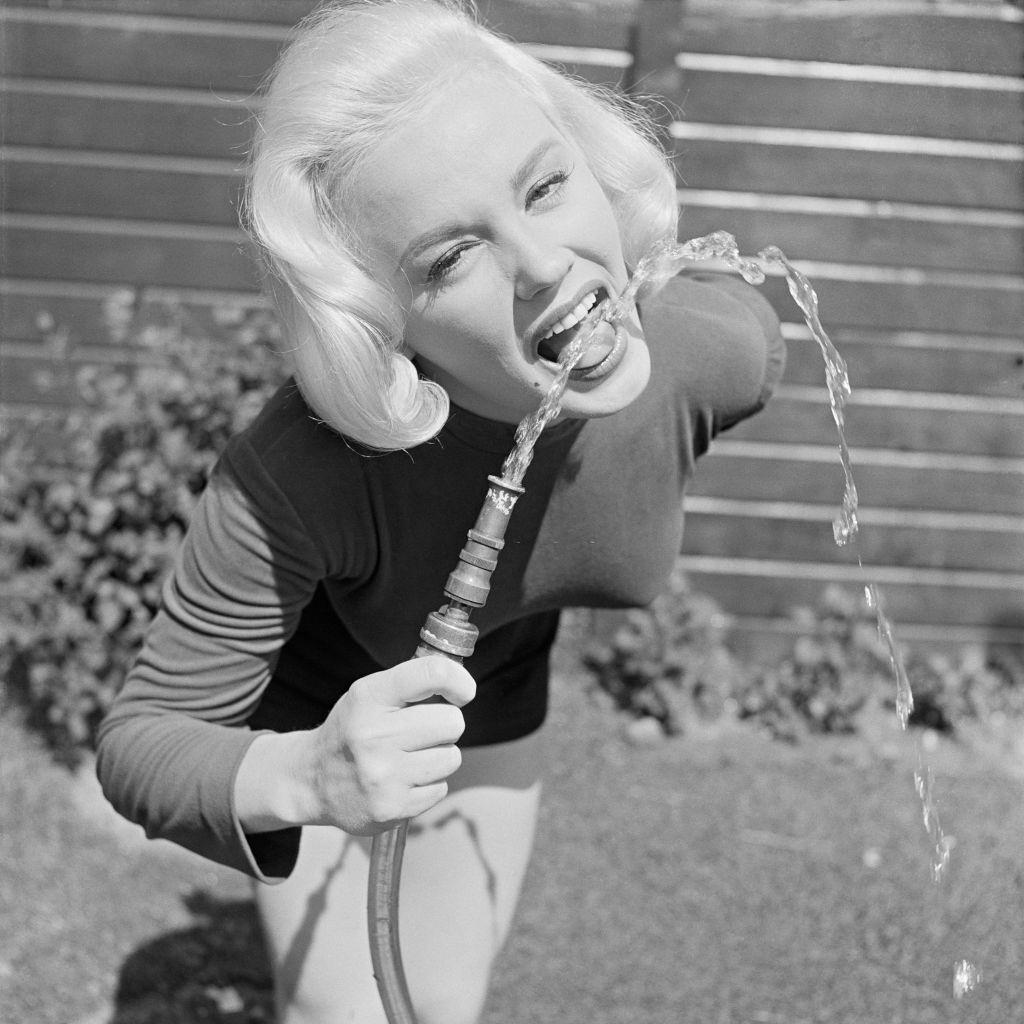 Mamie Van Doren drinking from a water hose and playing in the garden, California, 1954.