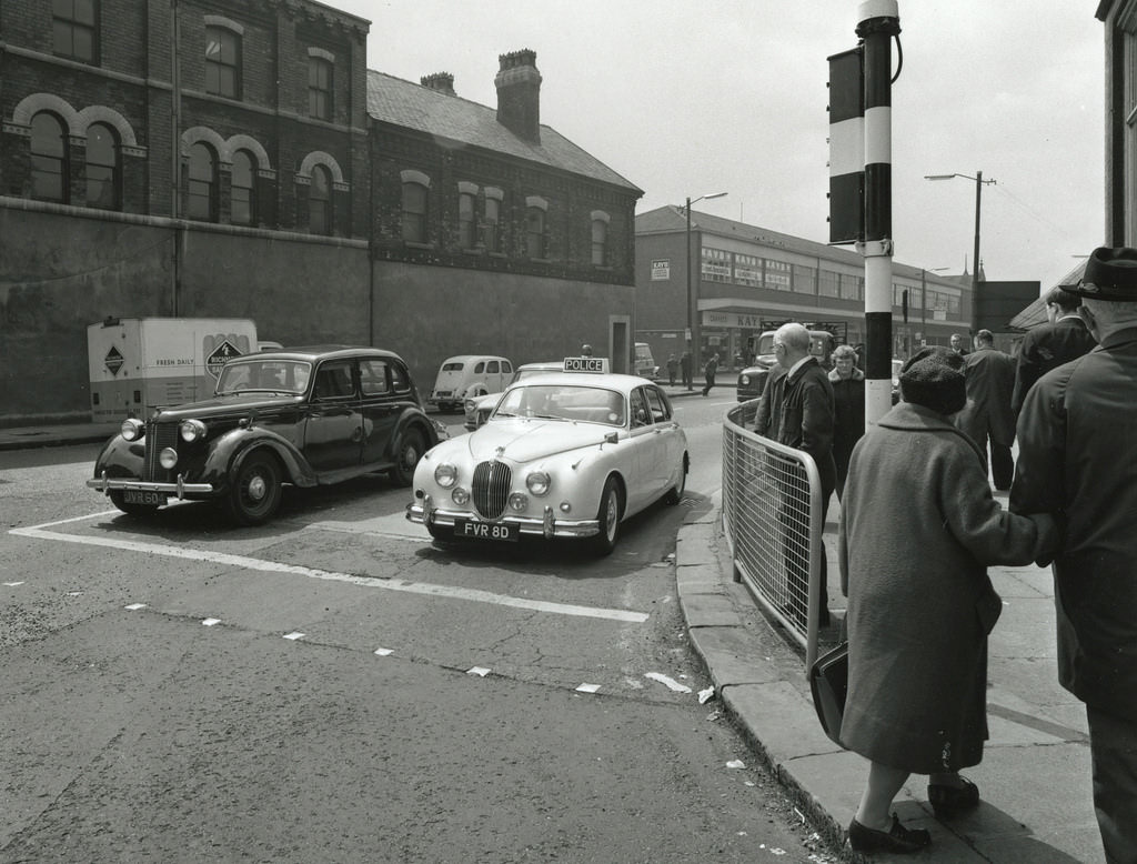 A Manchester City Police Mark 2 Jaguar waits at traffic lights while being driven through longsight in the 1960s
