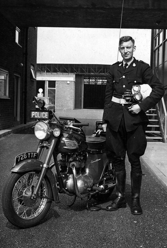 A Lancashire Constabulary motorcyclist stands proudly beside his Triumph machine in the rear yard of Ashton-under-Lyne Police Station in 1963