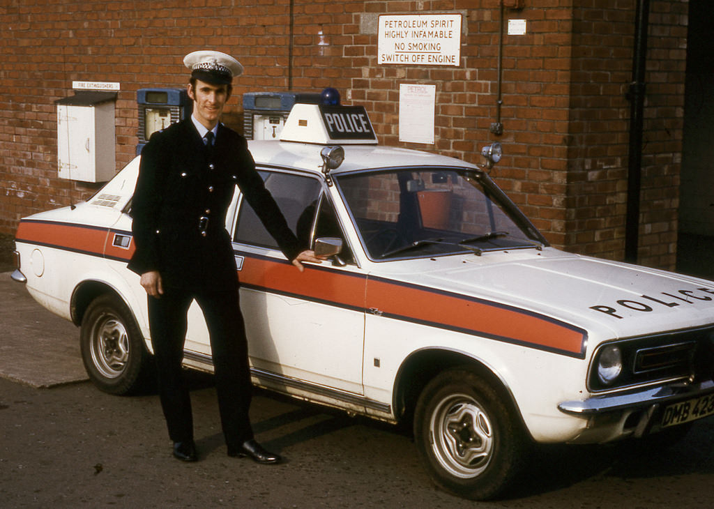 A police officer stands proudly beside his Morris Marina police car in the yard of Stretford Police Station sometime in the mid 1970s