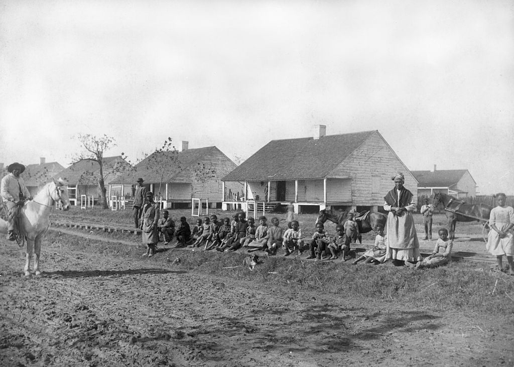 African-American children sit on the edge of a railroad by a dirt road, in a shantytown on the outskirts of New Orleans, 1880.