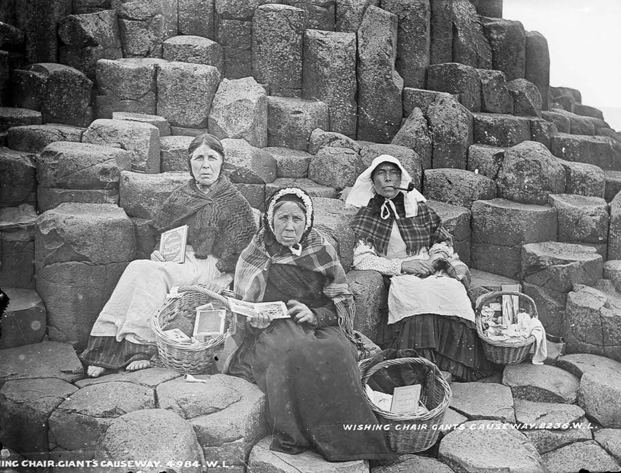 Women sell tourist trinkets and books on Fionn Mac Cumhaill’s Wishing Chair at the Giant’s Causeway, County Antrim, 1900.