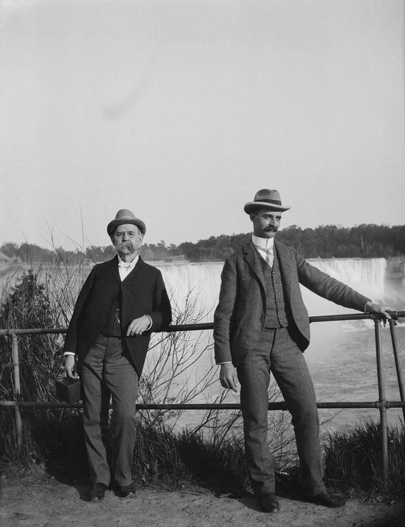 Two men standing besides railings overlooking Niagara Falls waterfalls on the Niagara river, ONtario, 1890s.