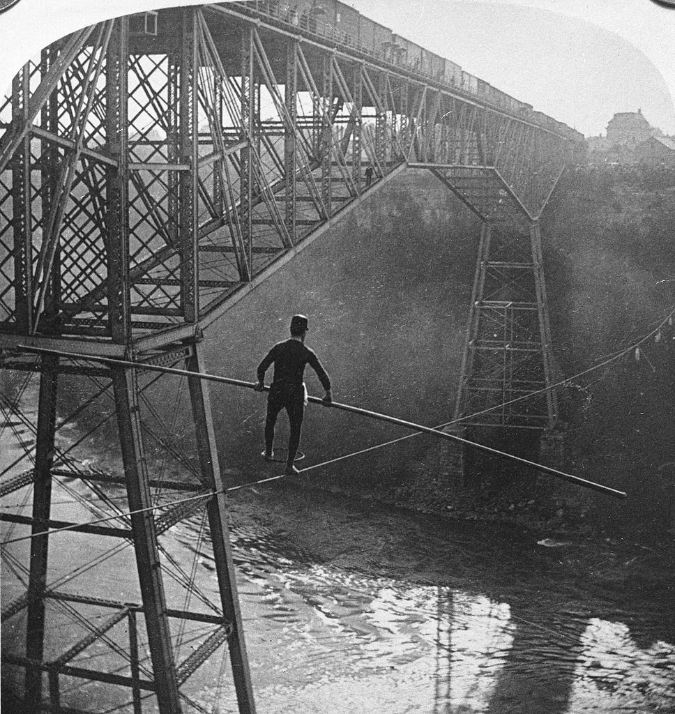 Funambulist Samuel Dixon balances himself with a pole while using Stephen Peer's cable to cross the Niagara Gorge towards Ontario,1890s.