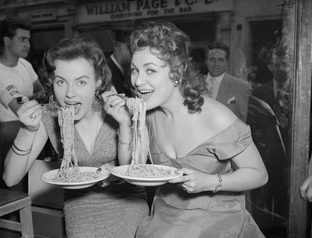 Mirv Arvinen (Miss Finland 1955) and Soho’s Fair Queen Andria Loran (right) try their hand at scoffing a plate of pasta at the Soho Fair spaghetti-eating contest on Frith Street, Soho, London in 1956.