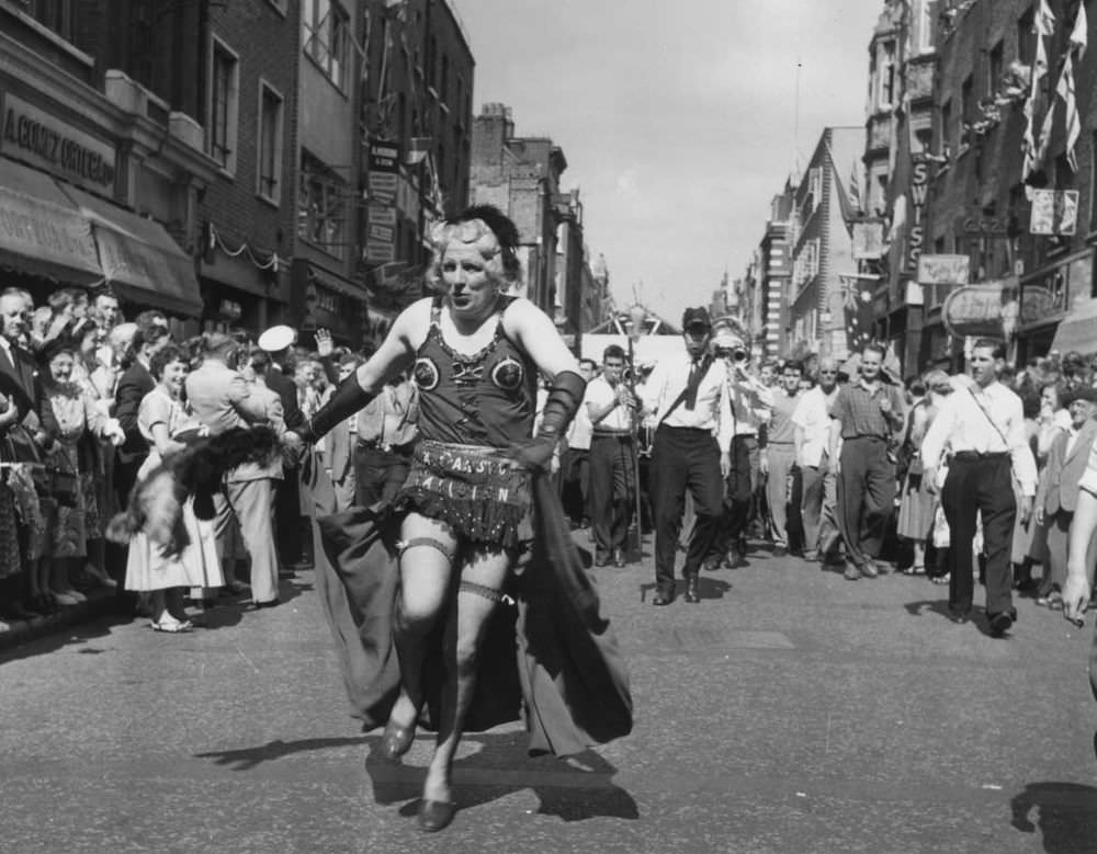 A man in drag heads a carnival procession down Old Compton Street during the Soho Fair in 1956.