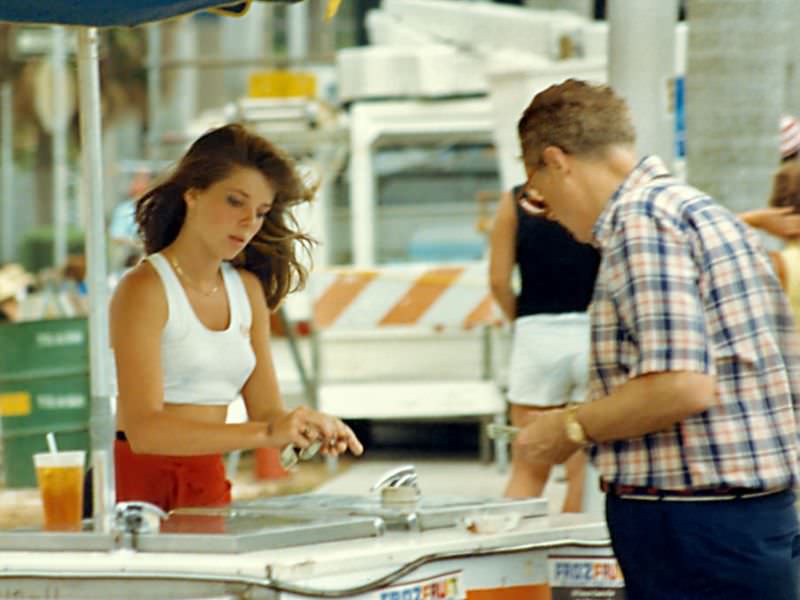 An attractive young lady makes change for a customer at a frozen snack cart, SunFest, 1988