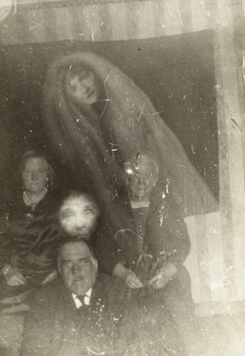 The spirits of an elderly woman and a younger woman appear over a group photo.