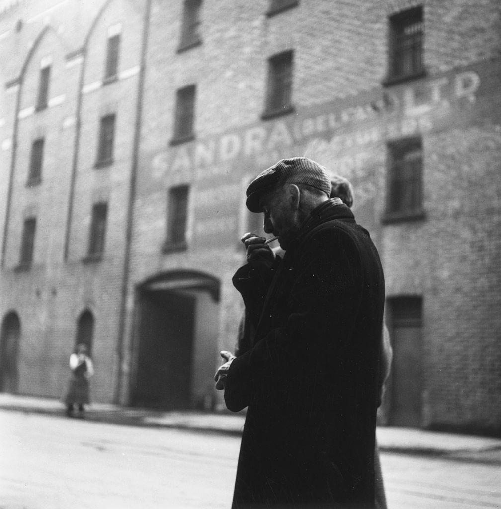 A man lighting up a cigarette in a Belfast street, 1954.