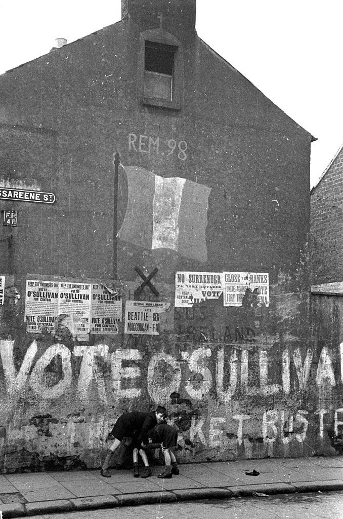 Boys playing on a street in Belfast underneath a spray painted message supporting O'Sullivan in a local election, 1954.