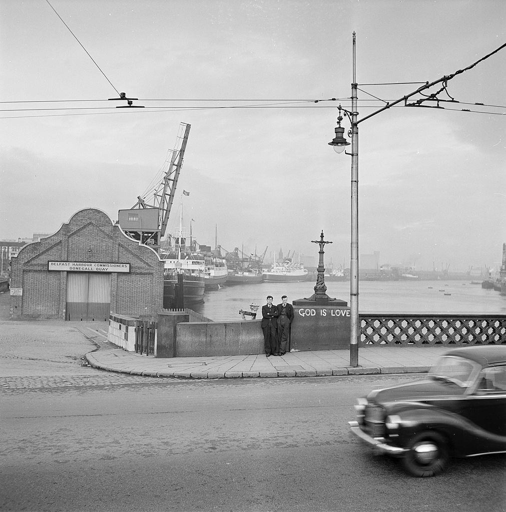 Two men are leaning against the low guardrail in Belfast, 1954.