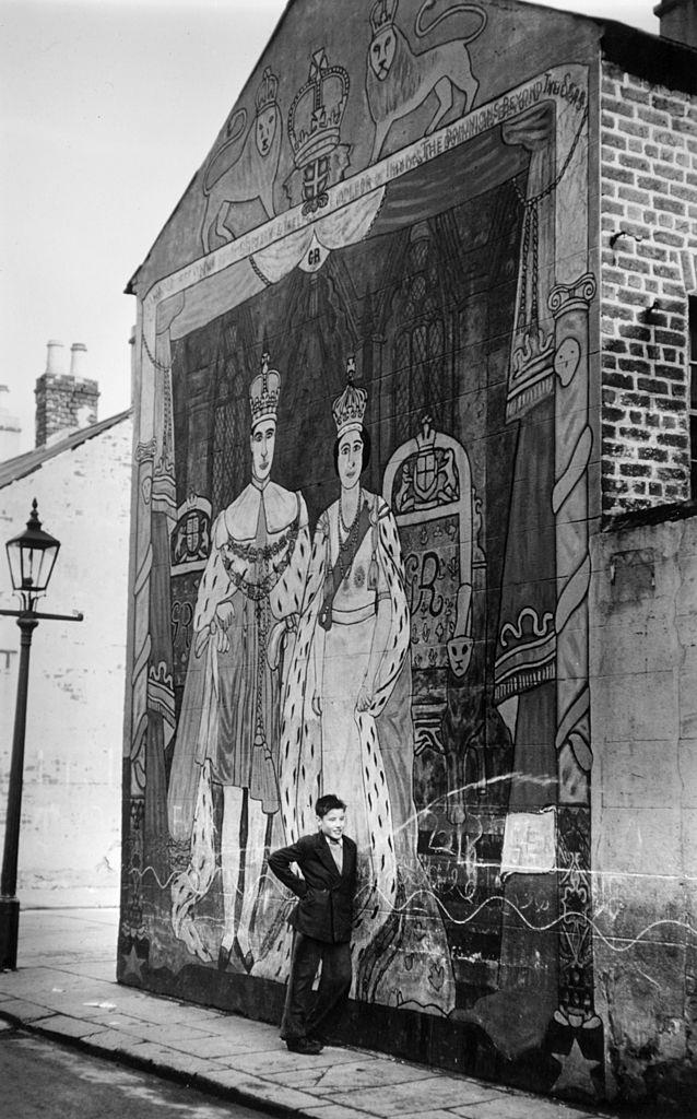 A young boy stands by a mural of Queen Elizabeth II and Prince Philip in Belfast, 1955.