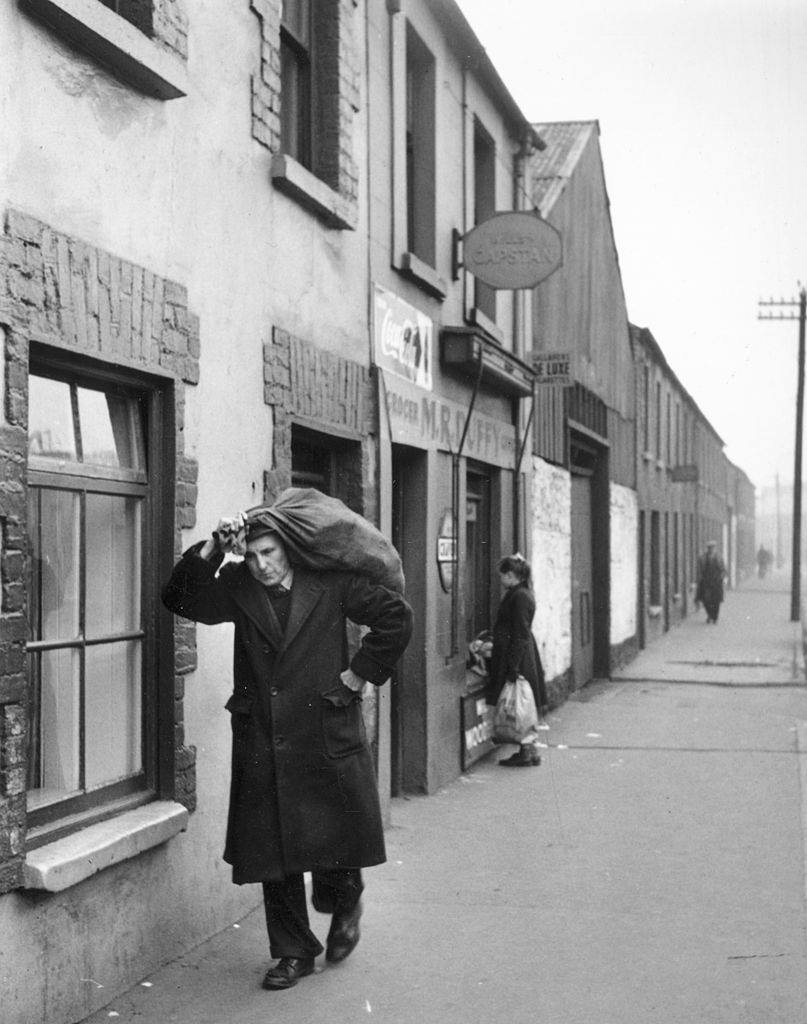 An unemployed Belfast man carrying a sack, 1955.