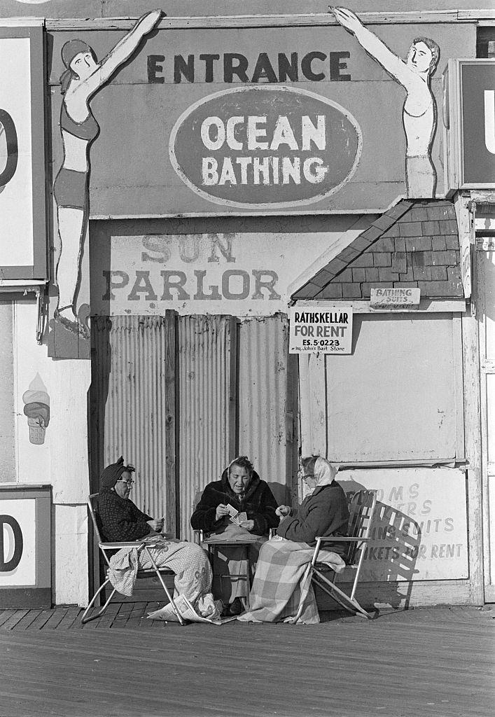 Bundled up against the cold, three elderly women play a game of cards in front of a bathhouse on the Coney Island boardwalk. December 11, 1959.