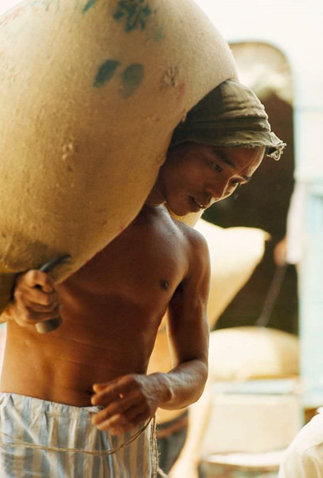 A man carries a large bag of rice on his back, Cholon, in Saigon, 1961