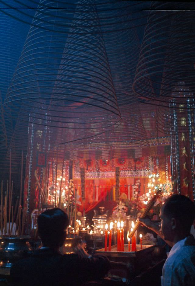 Burning incense and flickering candles cast a red glow on worshipers in Saigon, 1961