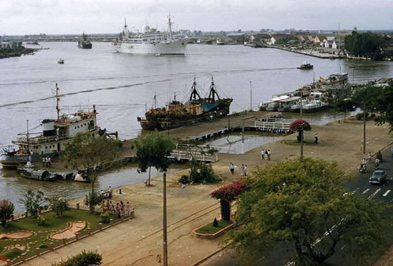 People promenade along the waterfront as large ships sail into port in Saigon, 1961