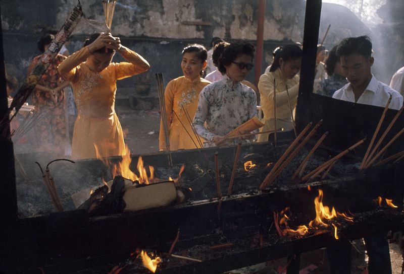 Women bow and pray by a fiery incense burner outside a temple in Saigon, 1961