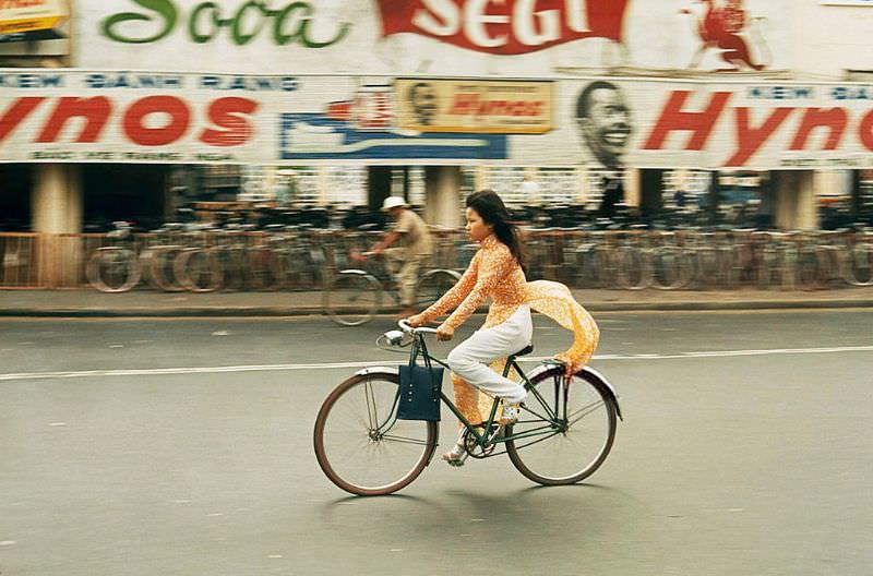 A woman ties down her ‘Ao dai’ while riding her bicycle in Saigon, 1965