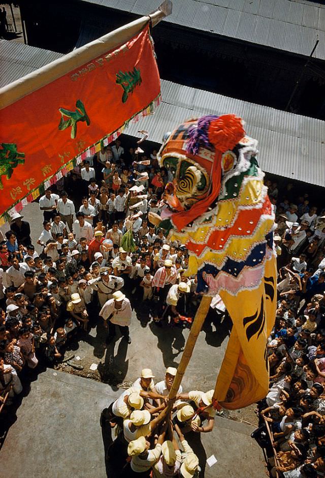 A costumed dancer climbs a pole to nab treats dangling from a banner, Cho Lon, 1961