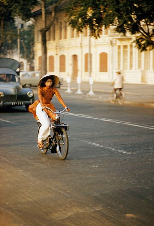 A girl in traditional clothes zips through traffic on a motorbike in Saigon, 1961