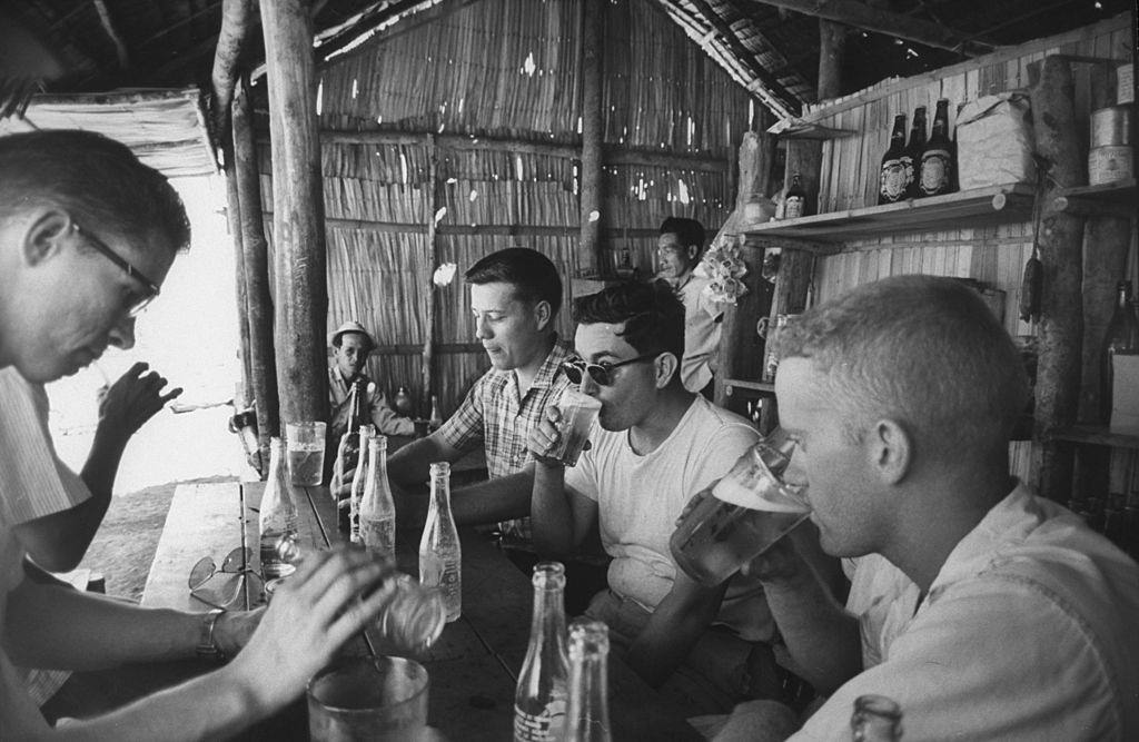 Volunteers drinking in thatched shack, 1961.