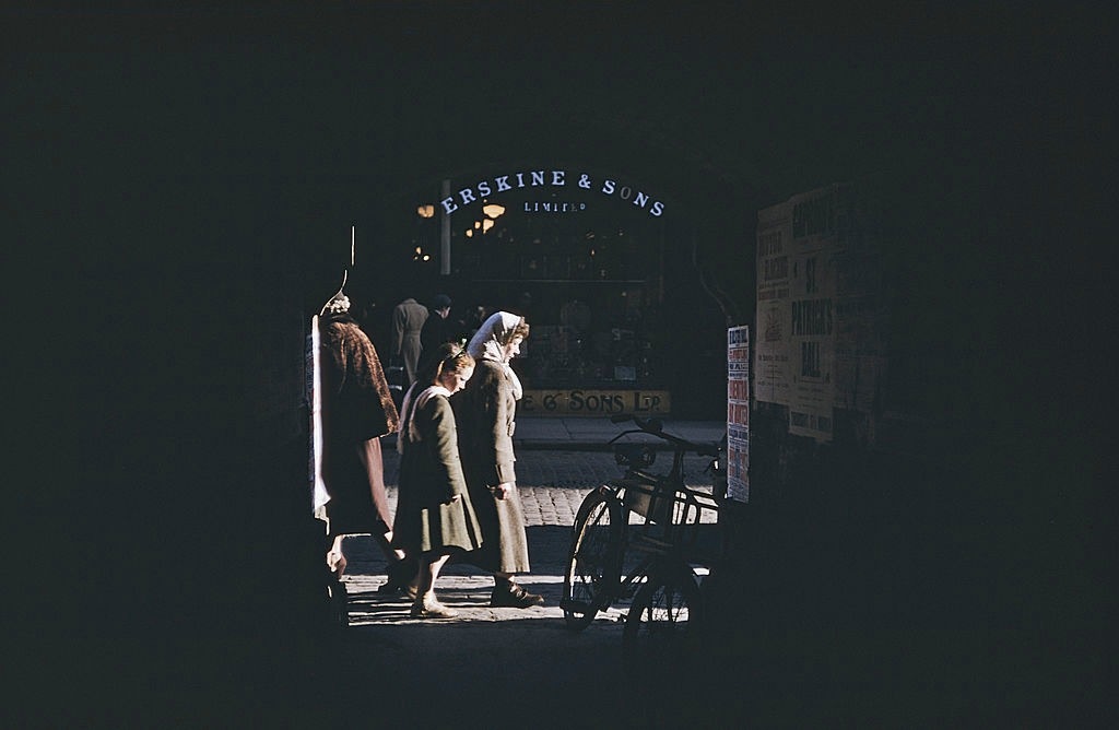 Pedestrians on a shopping street, seen through an archway, Belfast, 1955.