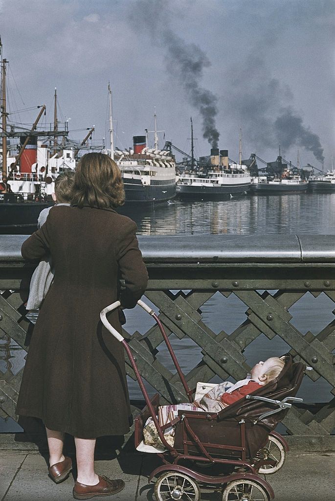 A woman with two children stops to look at shipping in a harbour, Belfast, 1955.