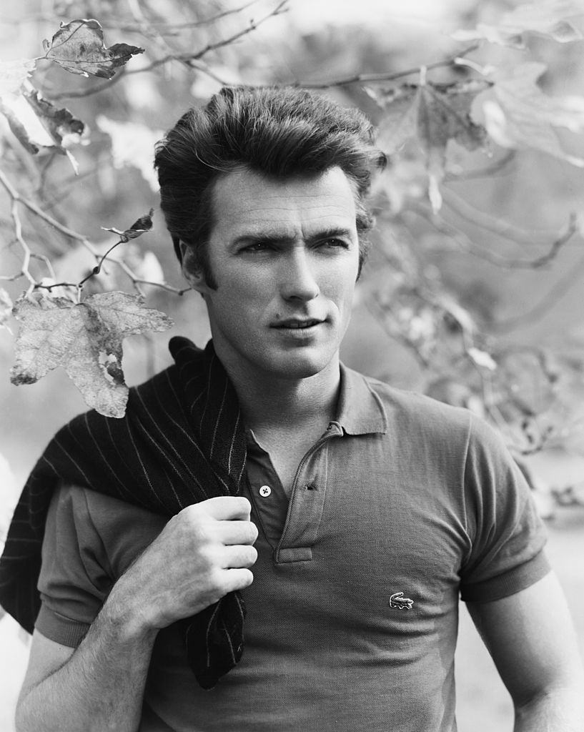 Clint Eastwood squinting while posing under a tree, with a sweater slung over his shoulder, 1960.