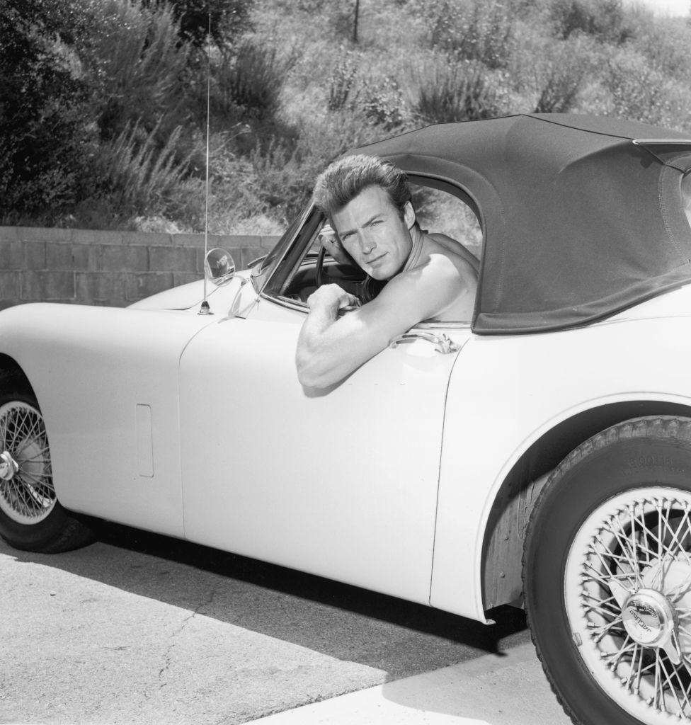 Clint Eastwood leaning out the window of a Jaguar convertible without a shirt, 1965.