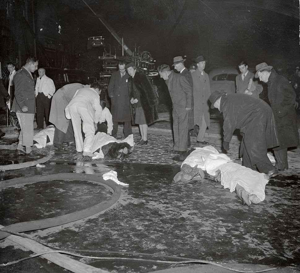 Bodies of four victims of the fire that destroyed Boston's popular Cocoanut Grove Night Club last night (November. 28) lie in the street, waiting removal to the city's overcrowded morgues.