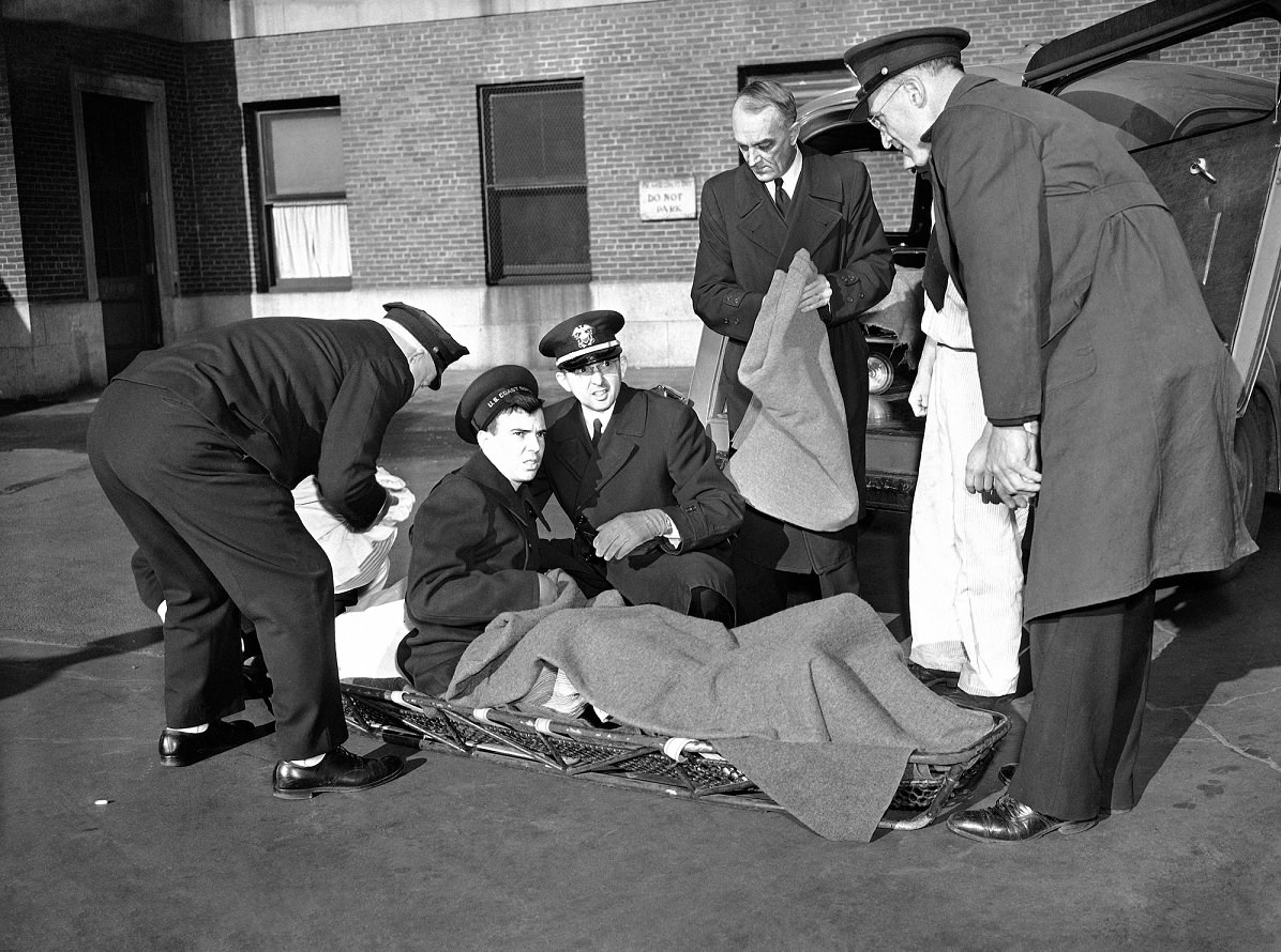 Surrounded by his Coast Guard buddies, Clifford Johnson, 22, of Sumner, Mo., lies on a stretcher outside Boston City Hospital, Nov. 26, 1943 after discharge as last victim of the Cocoanut Grove fire.