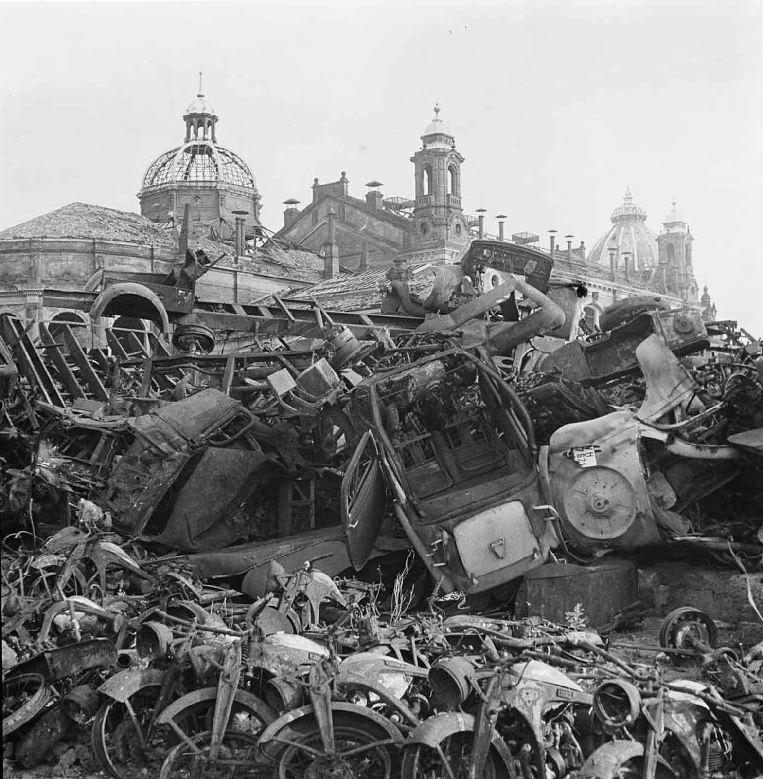 A provisional scrap yard with wrecked vehicles in front of the ruins of the exhibition palace in the Stübelallee in Dresden.