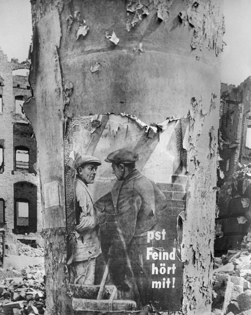 An advertising column with the remains of a Nazi poster which says "pst - Feind hört mit!", 1945.