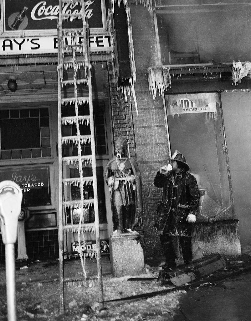 Firefighter looking at frozen ladder, 1900s.